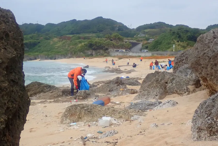 岩場と砂浜に散らばって漂着ごみを拾う参加者たち。手前にはペットボトルやポリタンクが流れ着いている